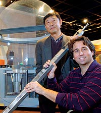 Physicist Won-Sik Yang and computer scientist Andrew Siegel hold a fuel rod assembly in front of a model of the Experimental Breeder Reactor-II
